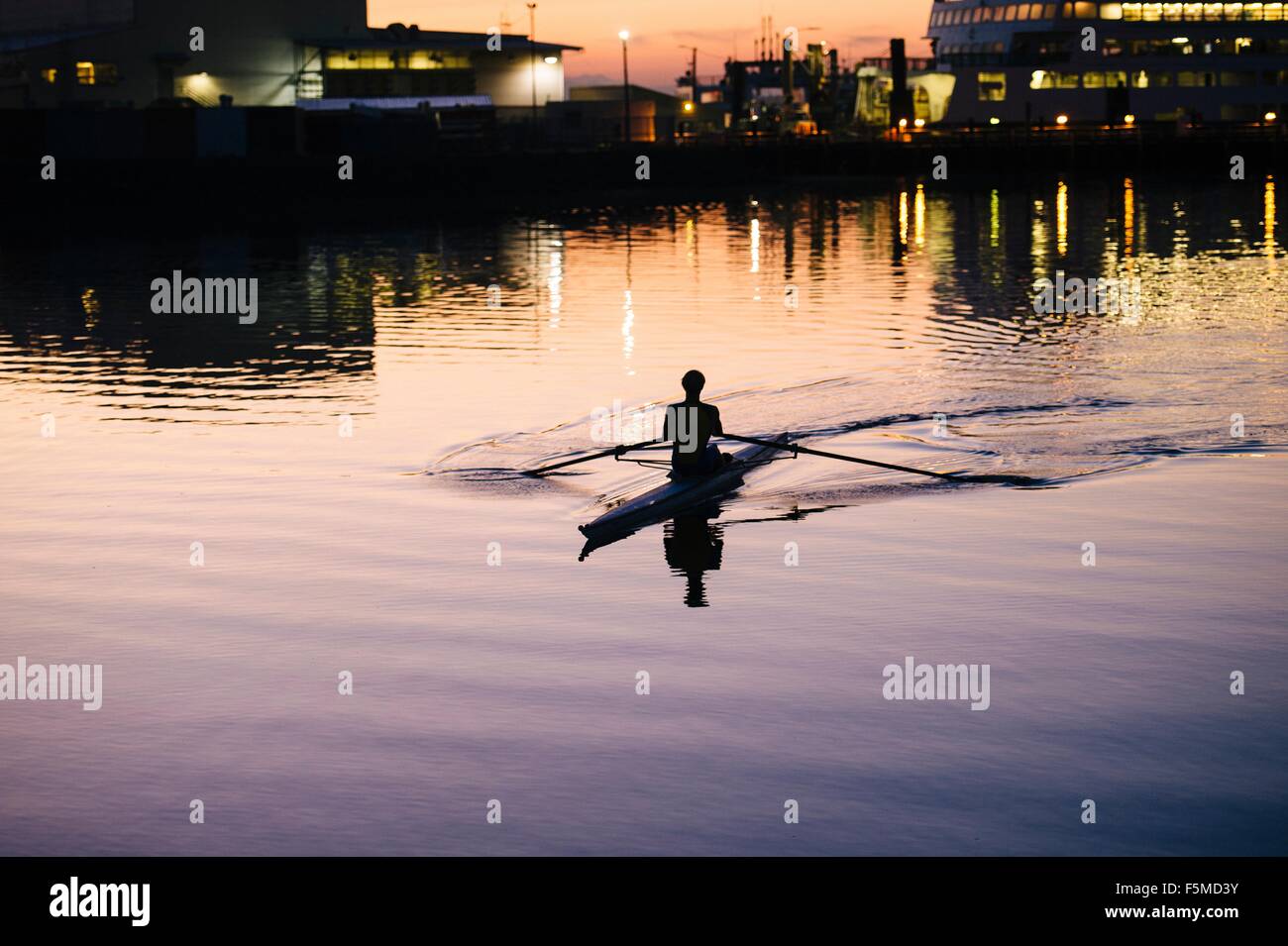 Young man rowing on river at sunset Stock Photo