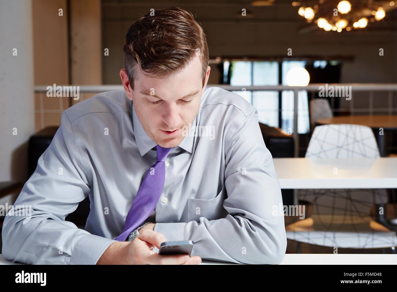 Mid adult businessman sitting at desk, looking at smartphone Stock Photo