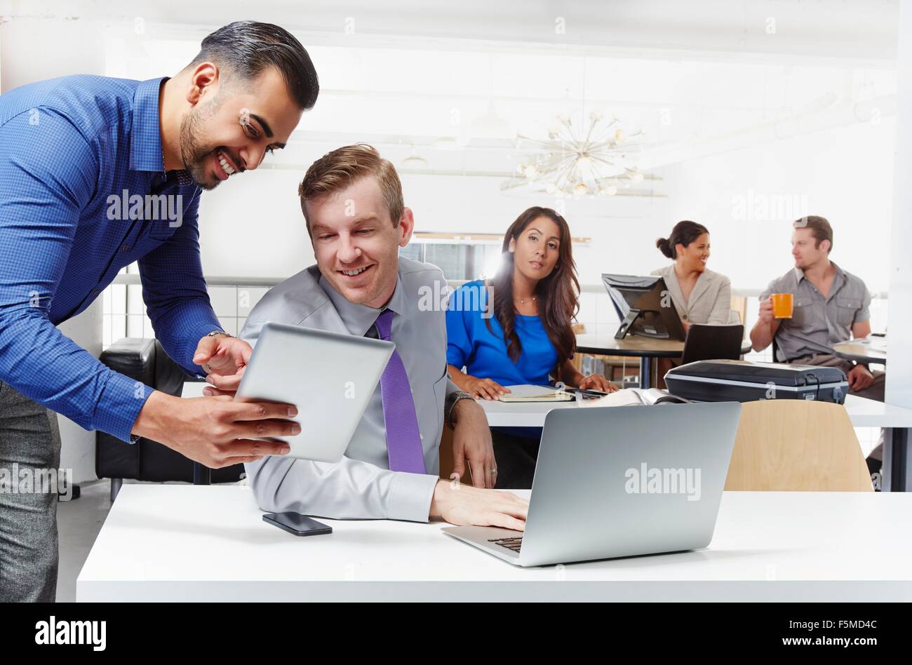 Two businessmen having discussion, looking at digital tablet, colleagues working in background Stock Photo
