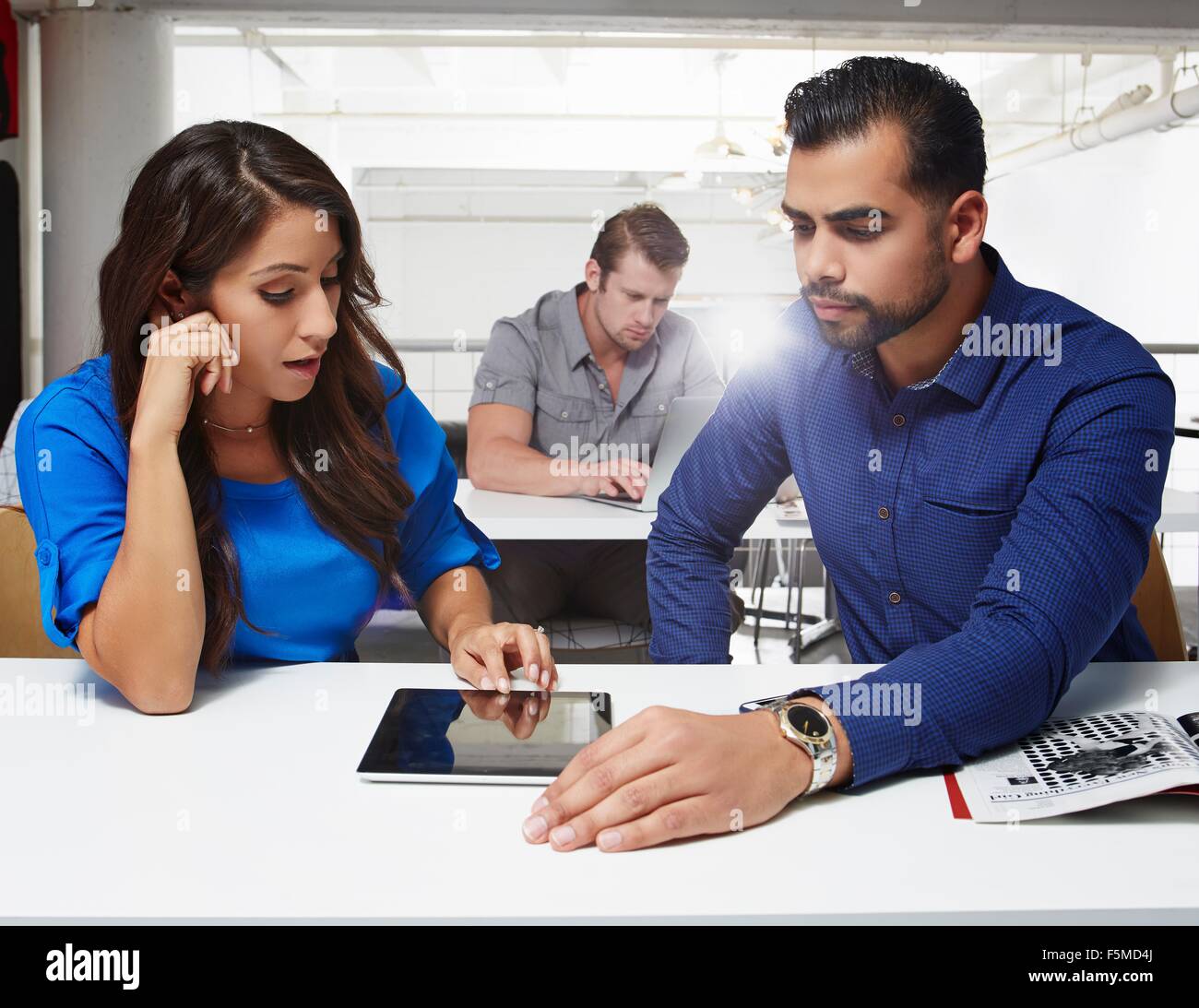 Businesswoman and businessman sitting at desk, looking at digital tablet Stock Photo