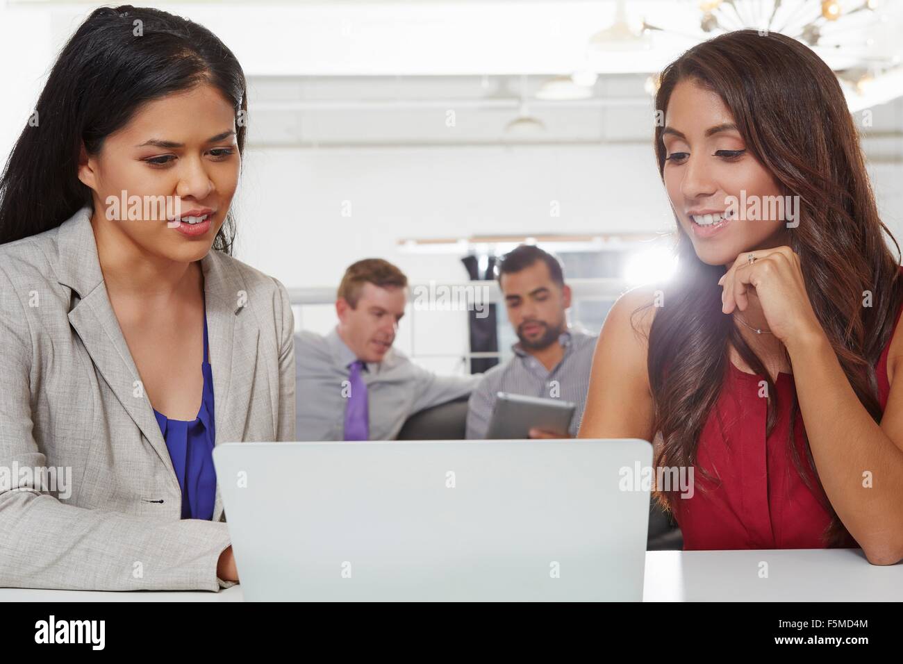 Two businesswomen sitting at desk, looking at laptop Stock Photo