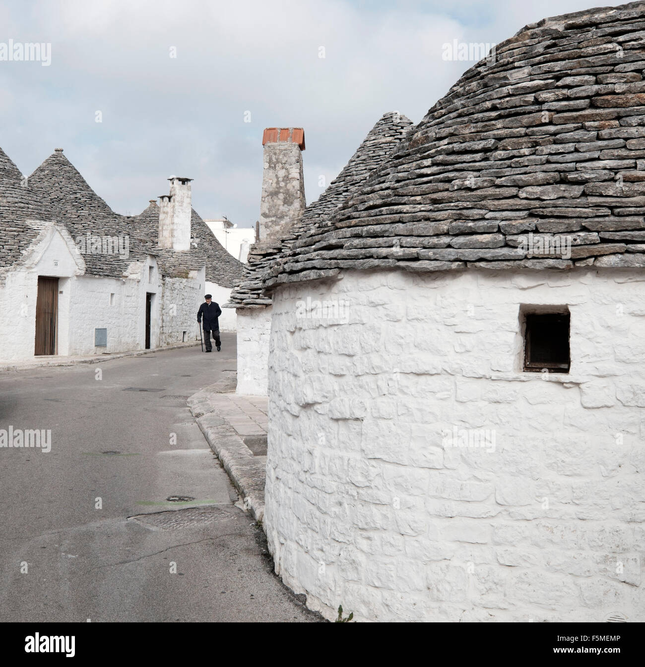 An elderly man walks down a street surrounded by the Trulli of Alberobello, Bari Province, Apuglia, Italy Stock Photo