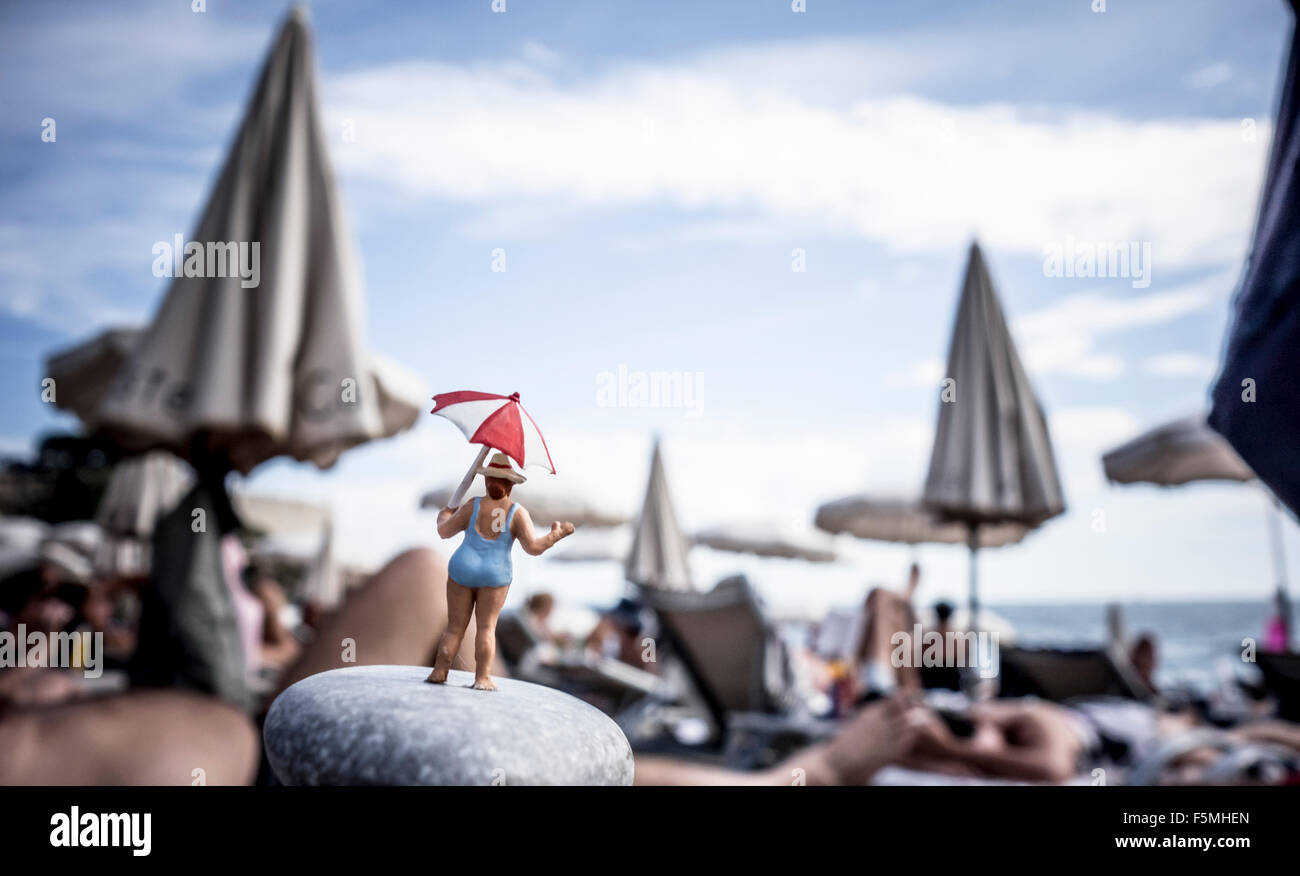 Rear view of a female figurine, standing on a pebble at the beach with an umbrella Stock Photo