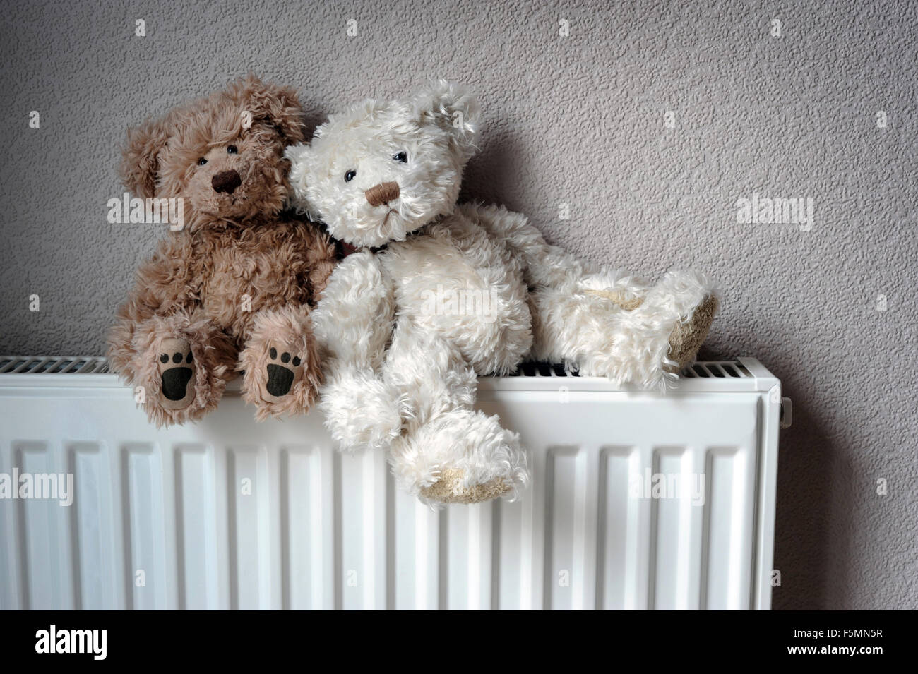TEDDY BEARS SITTING ON DOMESTIC RADIATOR RE HOMES CENTRAL HEATING WARM INSULATION HEATING WINTER FUEL BILLS COSTS GAS FUEL COSY Stock Photo