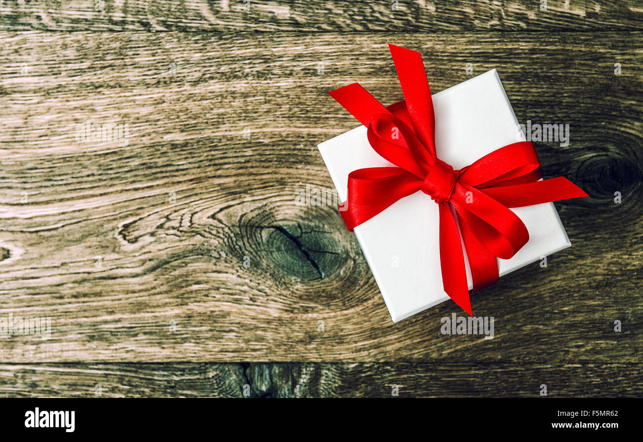 White gift box with red ribbon bow on wooden background. Vintage style ...
