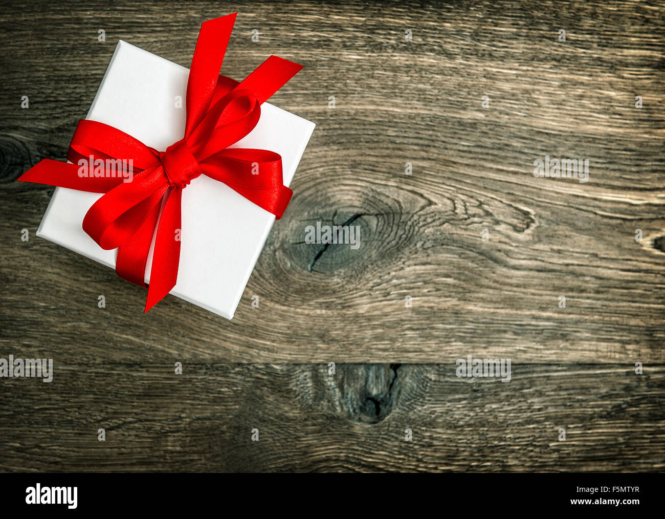 Gift box with red ribbon bow over rustic wooden background. Retro style ...