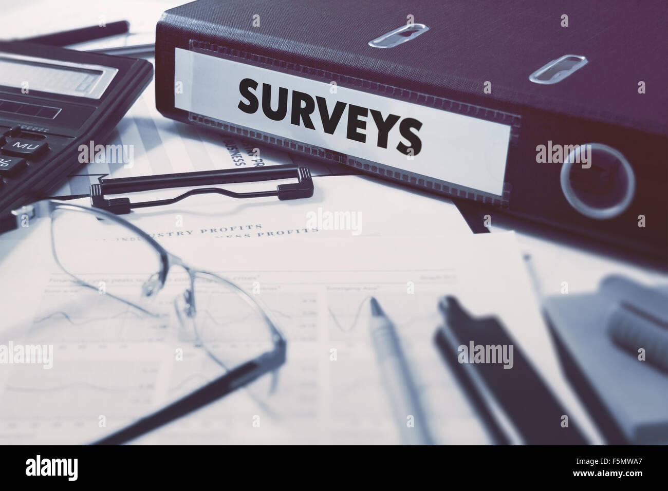 Ring Binder with inscription Surveys on Background of Working Table with Office Supplies, Glasses, Reports. Toned Illustration. Stock Photo