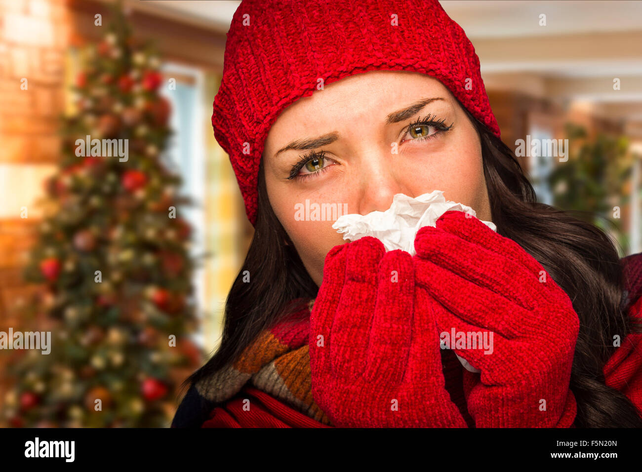 Sick Mixed Race Woman Blowing Her Sore Nose With Tissue In Christmas Setting. Stock Photo