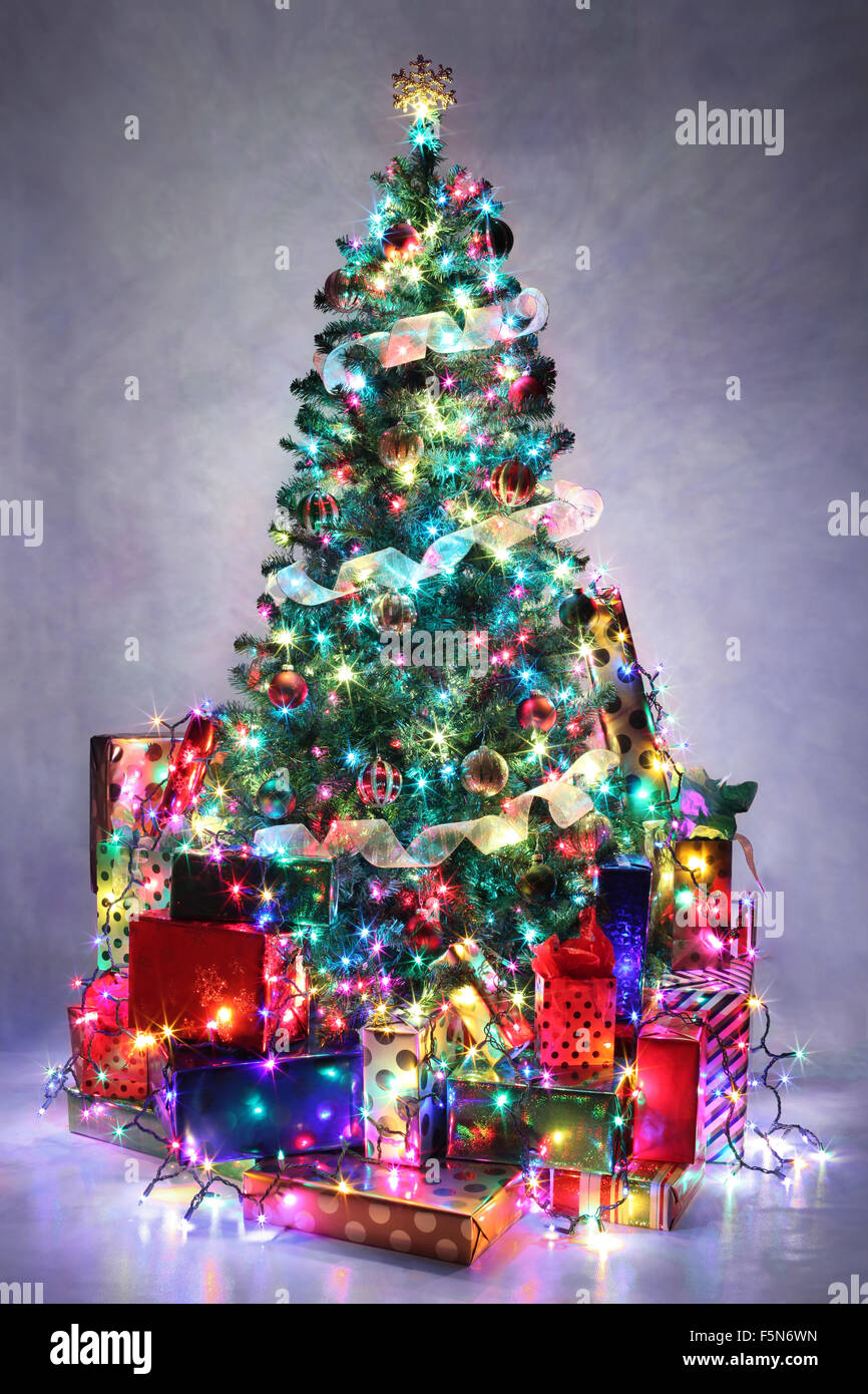 Decorated Christmas tree with colorful lights surrounded by presents. Stock Photo