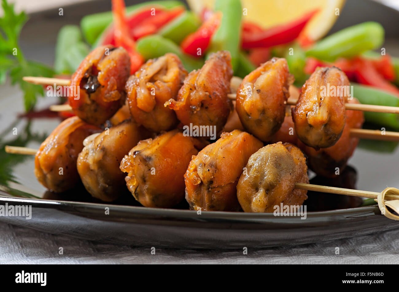 Fried mussels with onions on skewers c garnish of green beans and paprika Stock Photo