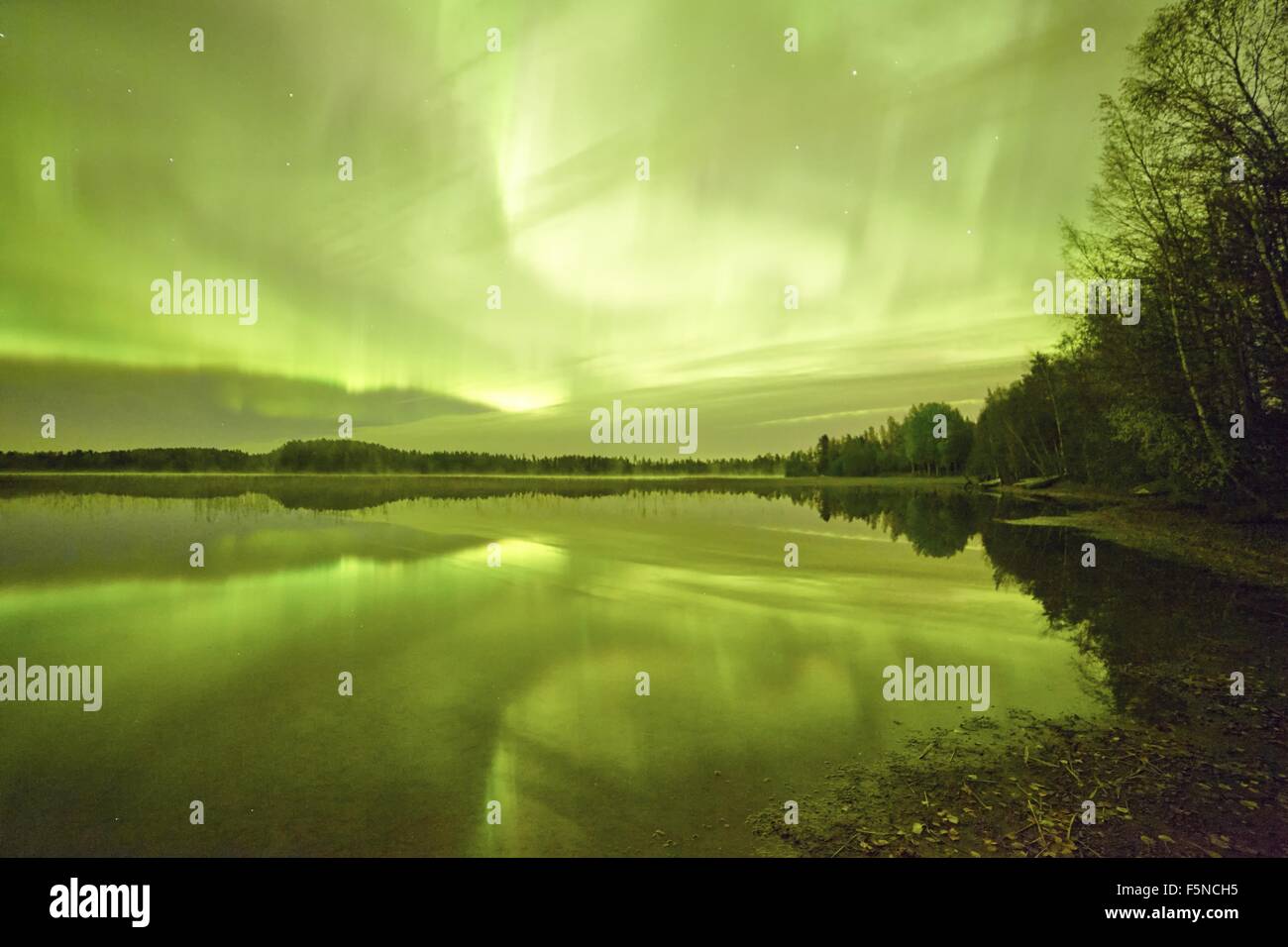Northern lights (Aurora Borealis) glowing in the night sky over a beautiful lake in Finland. Surreal landscape with vibrant colo Stock Photo