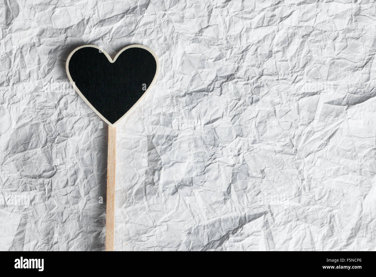 Wooden pointer in the shape of a heart  lying on a crumpled paper, as background Stock Photo