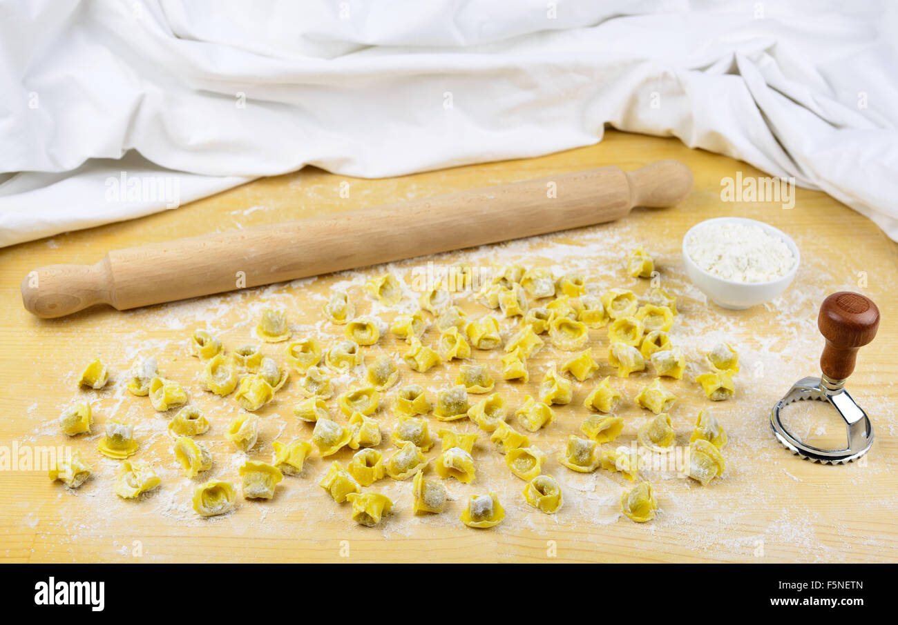 Tortellini emiliani homemade italian raw pasta stuffed with beef and pork meat, rolling pin, flour in a cup and on a wooden back Stock Photo