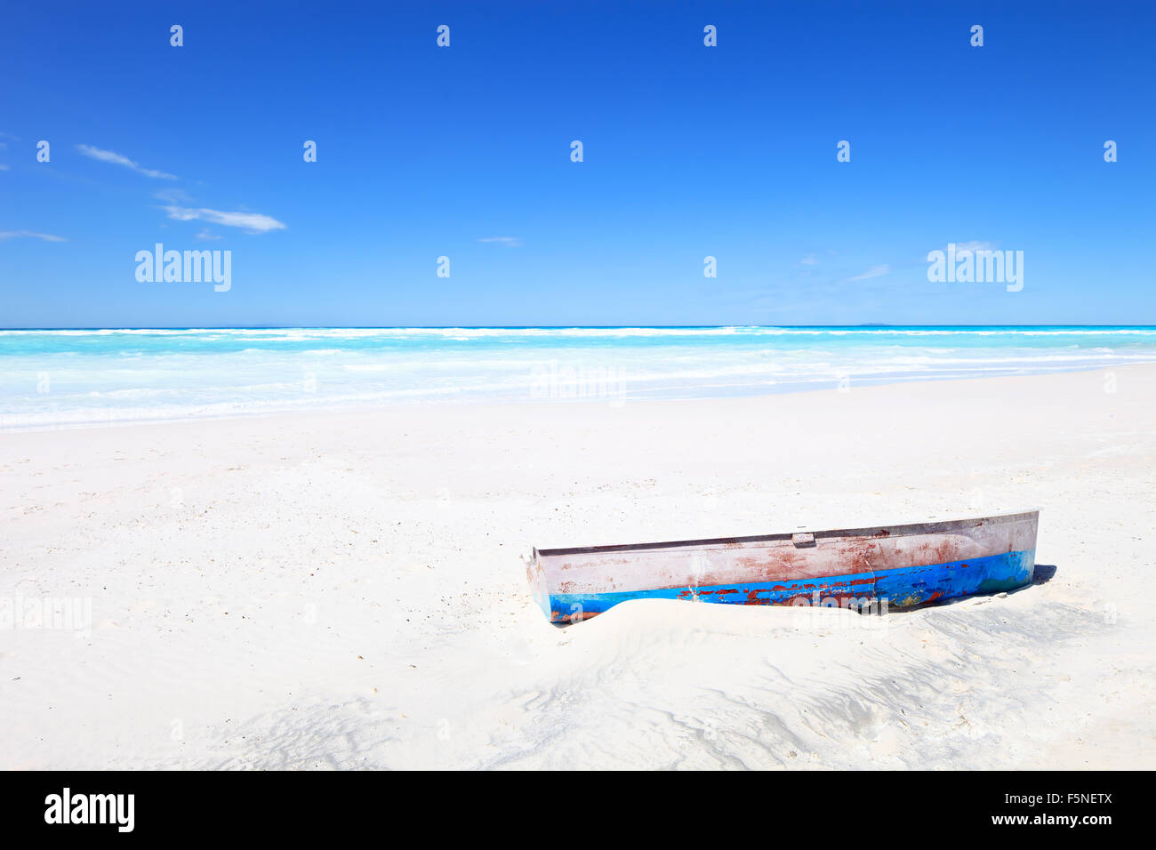 Tropical Seascape with an wooden, old and broken boat on white and sunny beach under a blue sky. Stock Photo