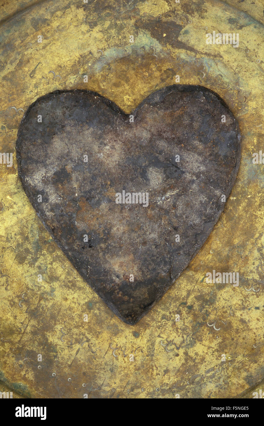 Heart-shaped grey slate with brown rust markings lying on tarnished patterned brass tray Stock Photo