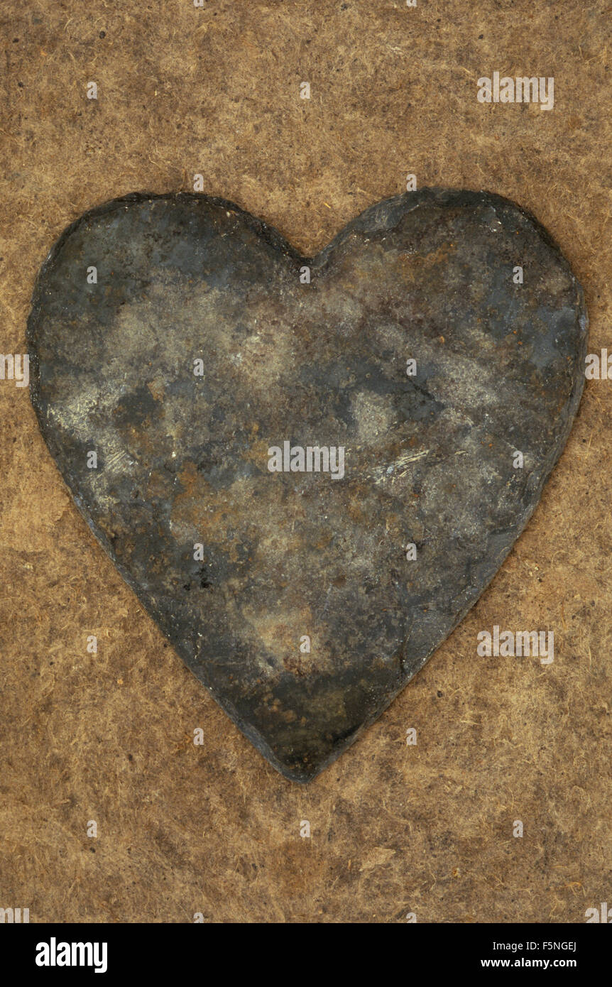 Heart-shaped grey slate with brown rust markings lying on antique board Stock Photo