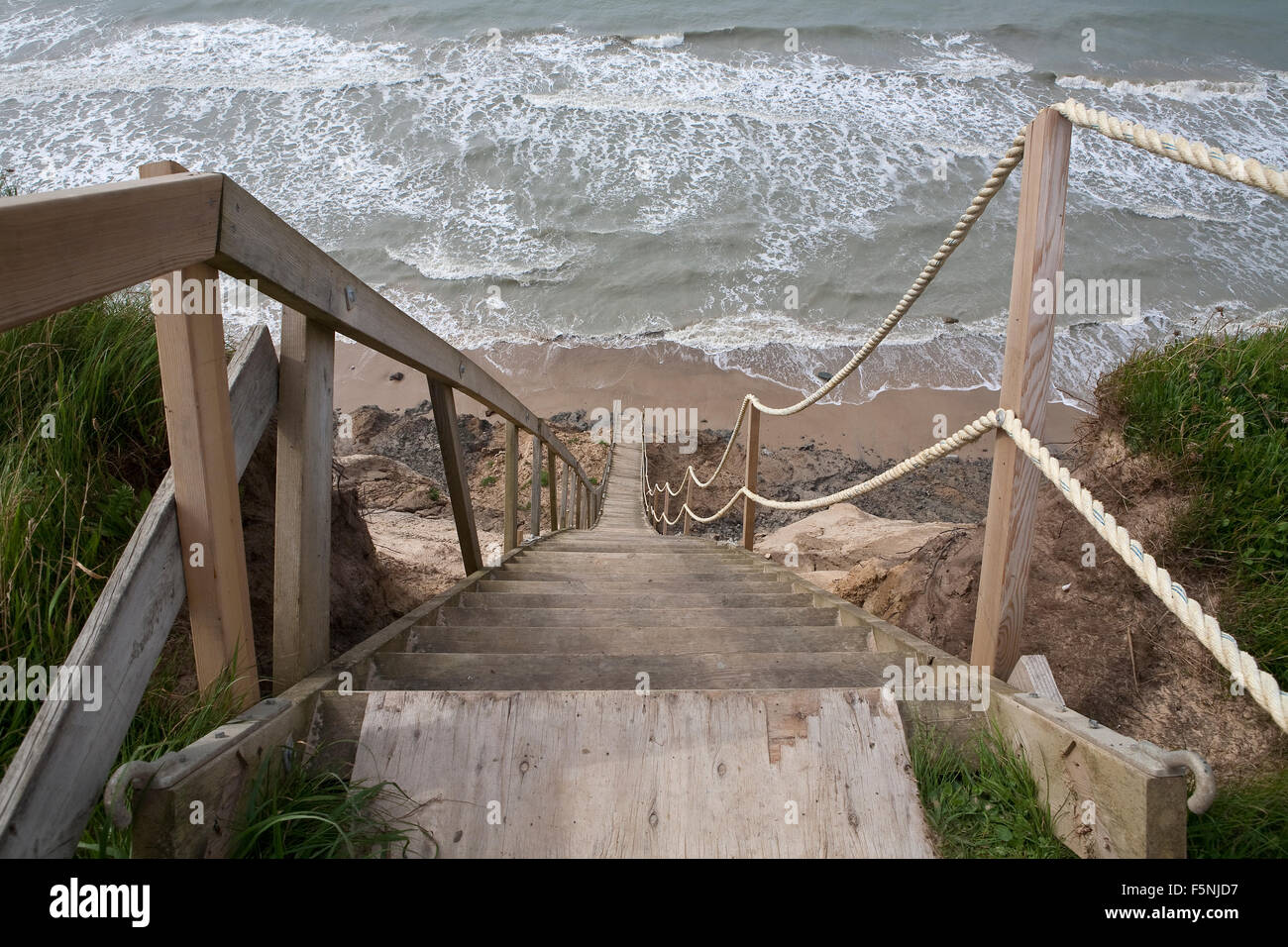 A steep staircase traverses an unstable cliff side to get people down to the sea shore. It is a long way down. Stock Photo