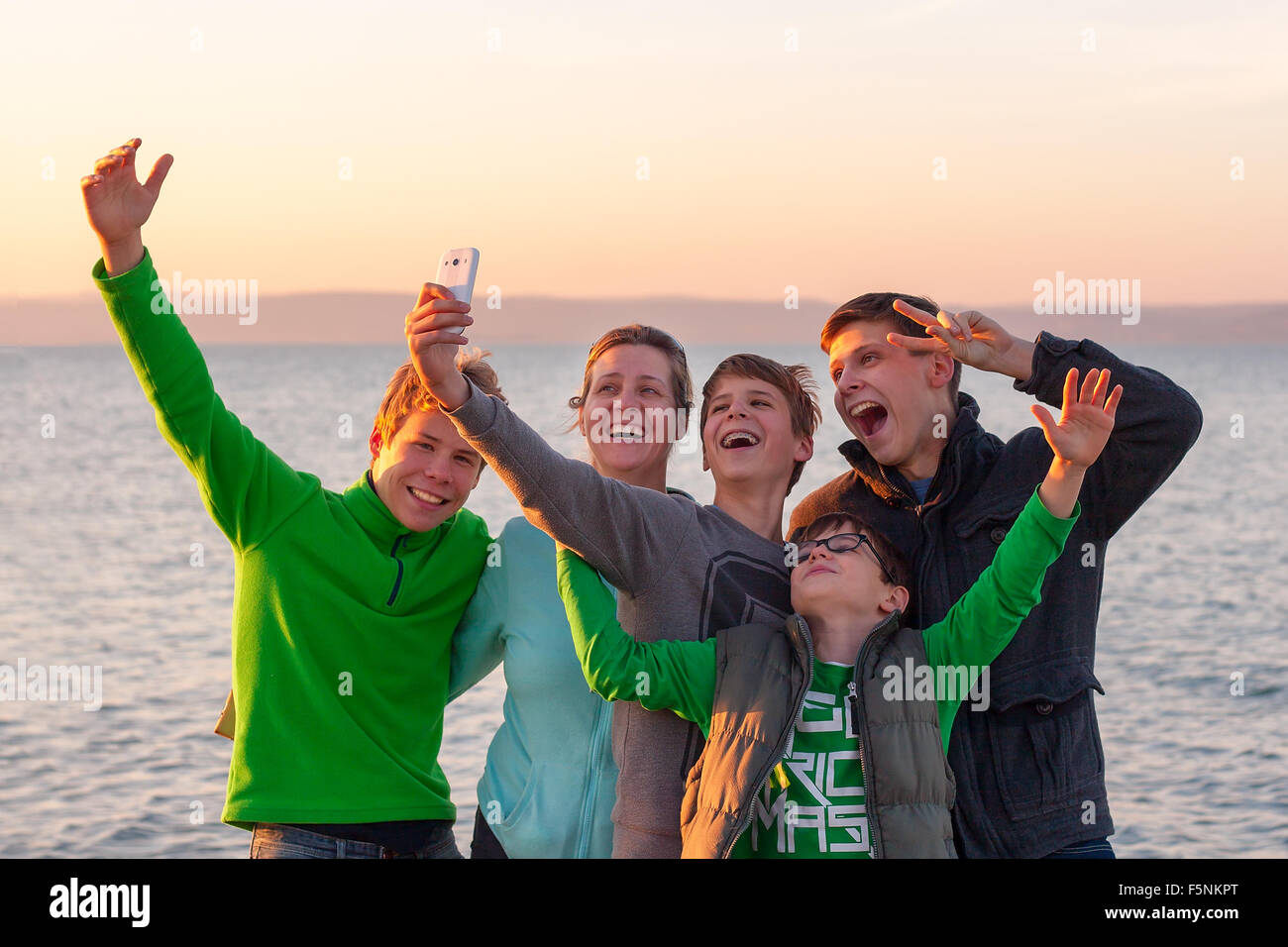 Group of happy young people taking a selfie with a white smart phone in front of a lake Stock Photo