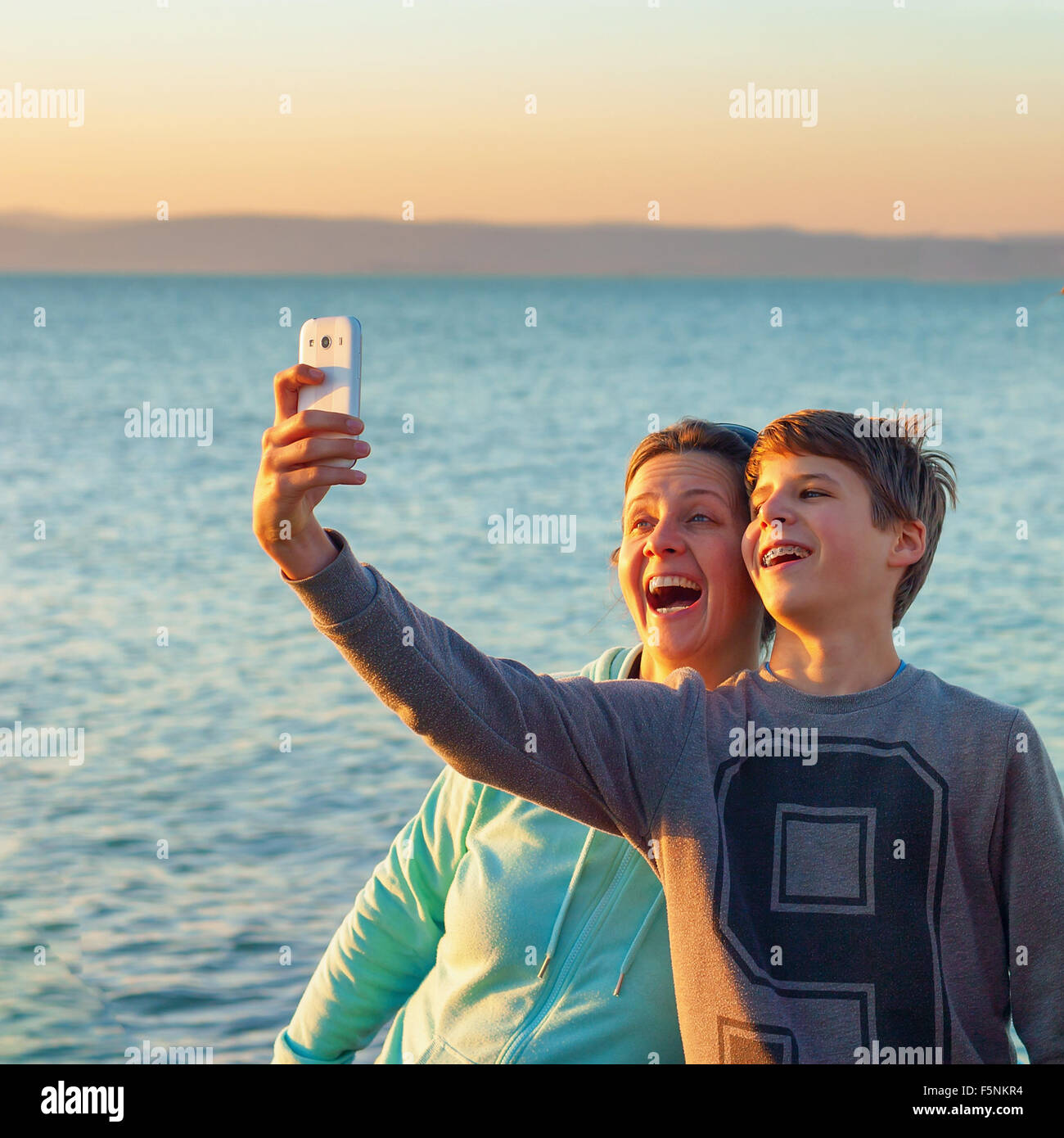Young boy and a happy adult woman taking a selfie in front of a lake the boy has braces on his teeth Stock Photo