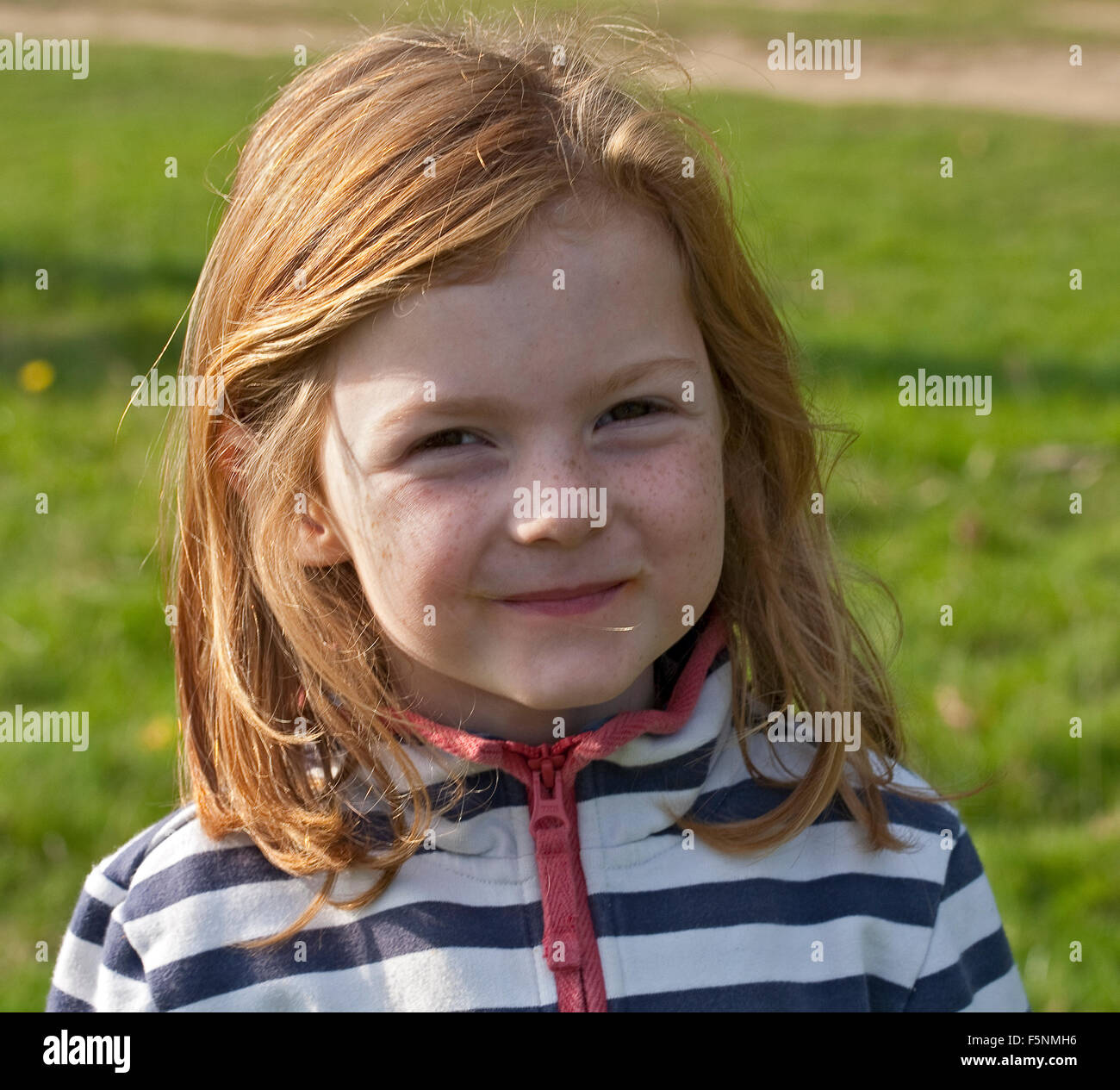 A young girl lit from the side is smiling beautifully at the camera. She has ginger hair which glows in the sunlight. Stock Photo