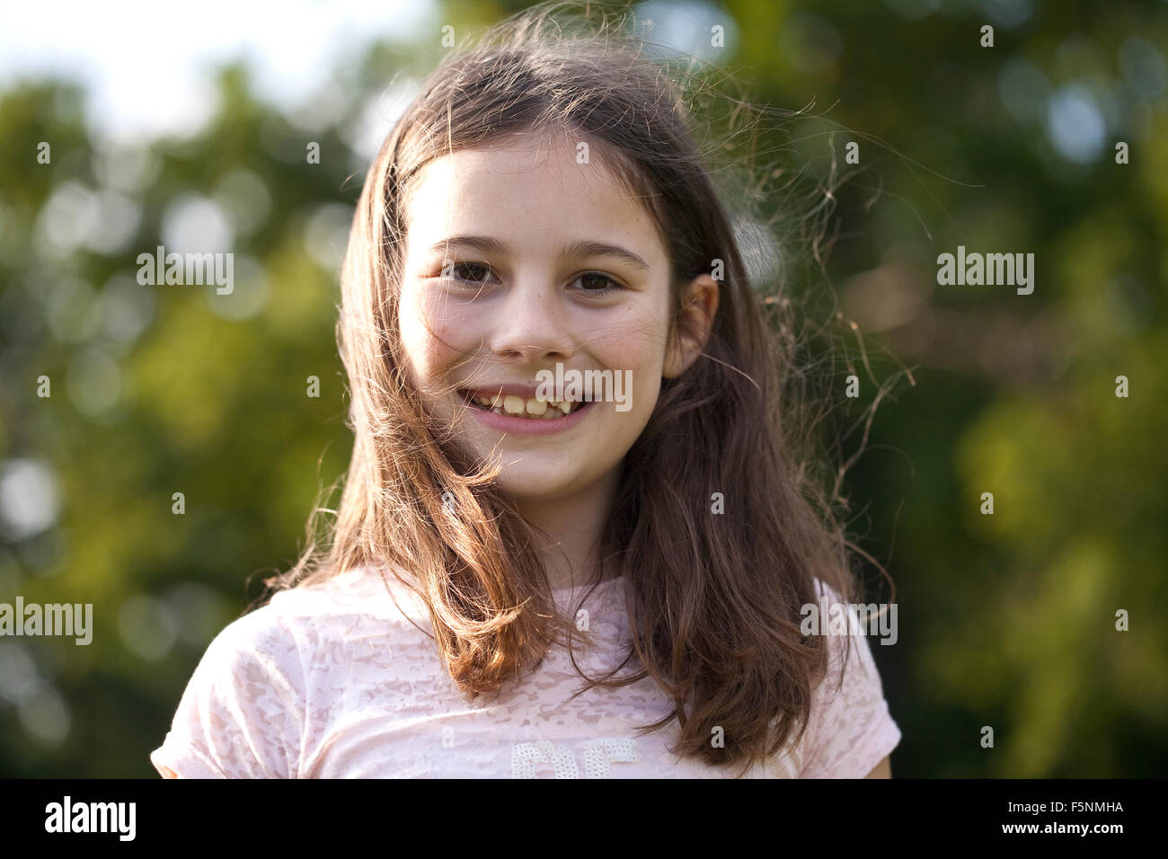 A young girl is smiling down at the camera. Her fine dark hair is dancing around her face. She has dark eyes and a big smile. Stock Photo