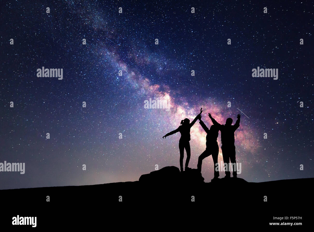 Milky Way. Night sky with stars and silhouette of a happy family with raised-up arms Stock Photo