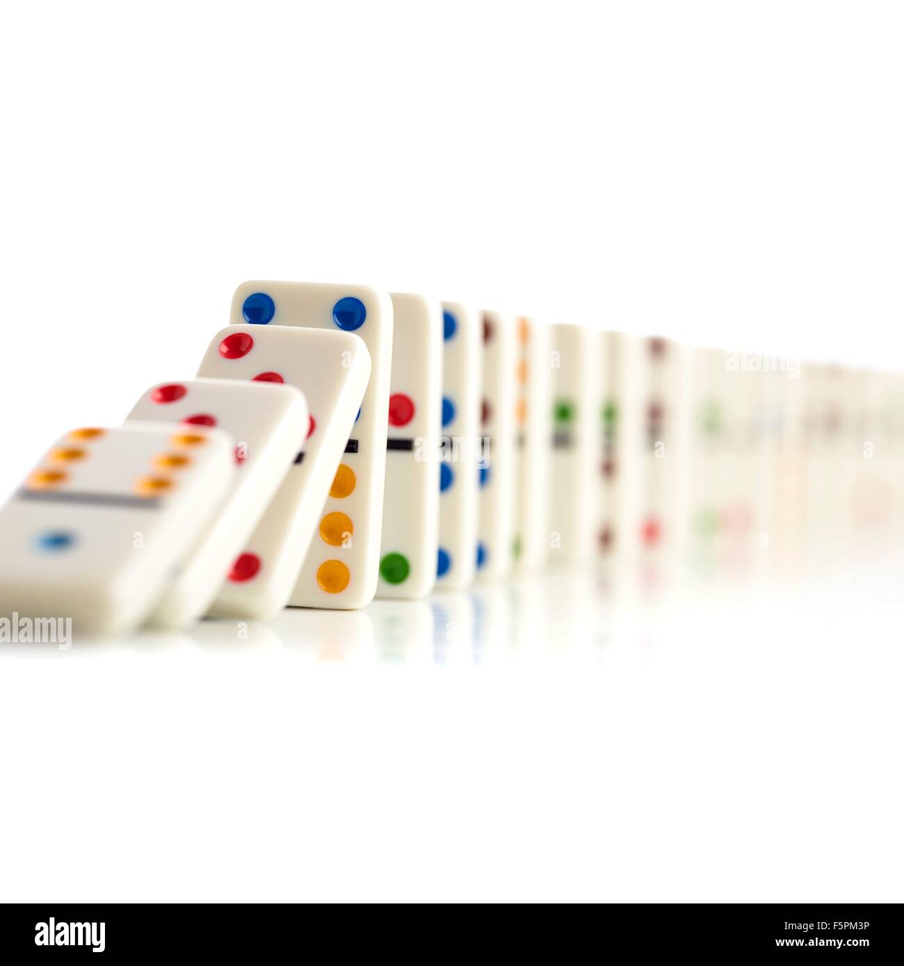 Colourful dominoes falling down against a white background. Stock Photo