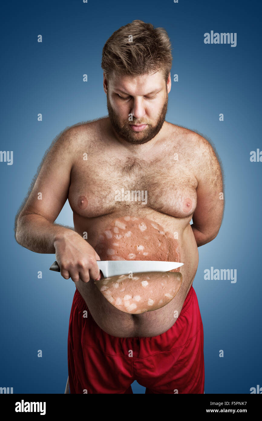 Fat man cuts a big slice of a sausage from his belly over blue Stock Photo