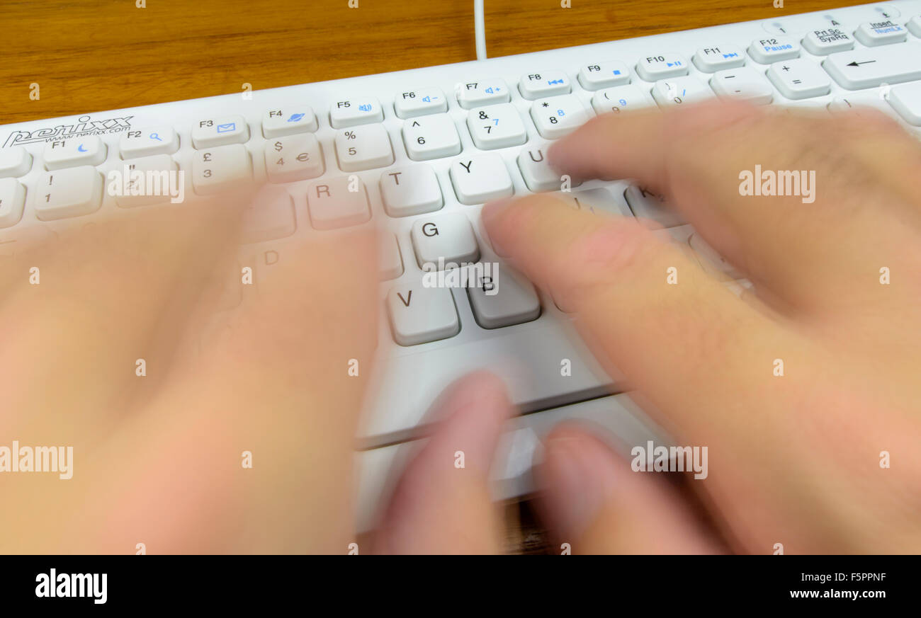 Typing fast on a computer keyboard, with the typists hands blurred to infer speed. Stock Photo