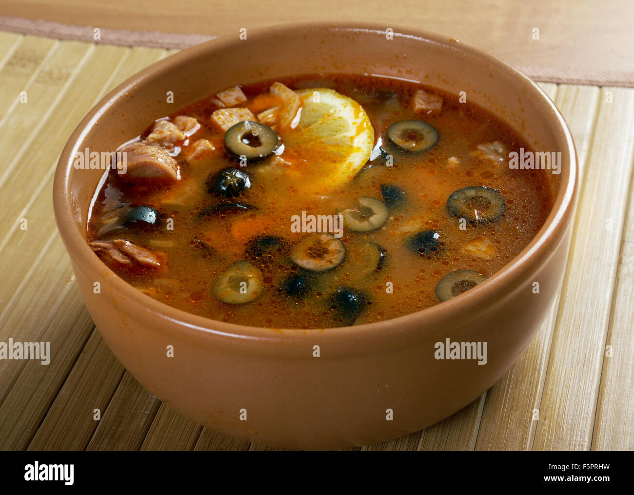 Solyanka on the plate.Solyanka, Russian soup with beef,sausage,chicken and lemon, olives Stock Photo