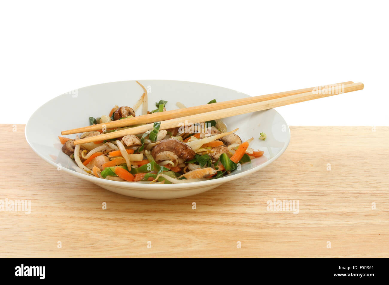 Stir fried chicken abd vegetables with chopsticks in a bowl on a wooden table Stock Photo