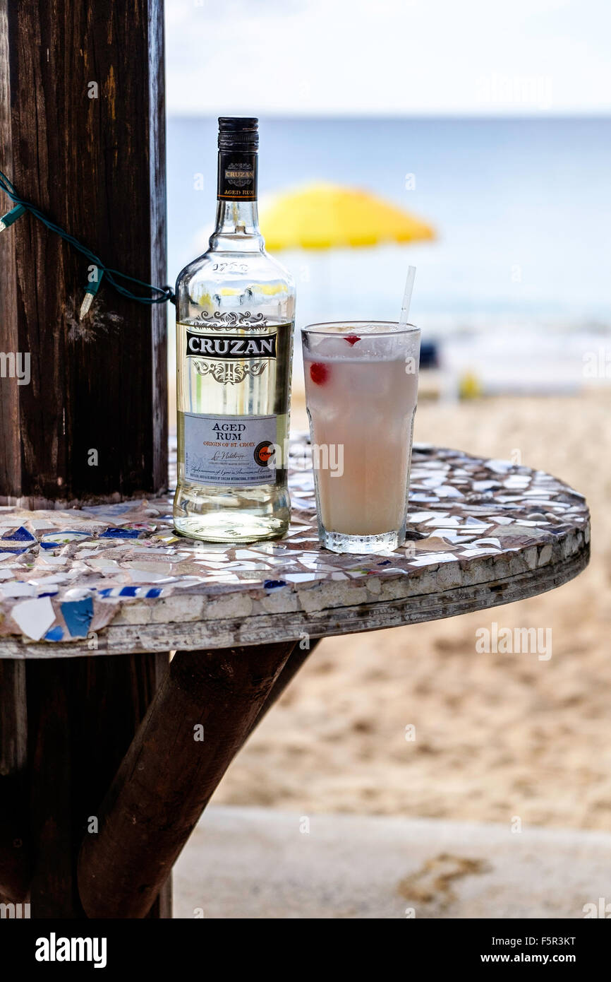 A bottle of Cruzan aged rum and a rum cocktail in a glass, Caribbean sea in the background. Stock Photo