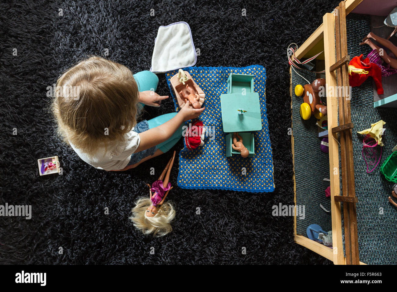 Little girl playing with dolls on a dark carpet inside at home. Stock Photo