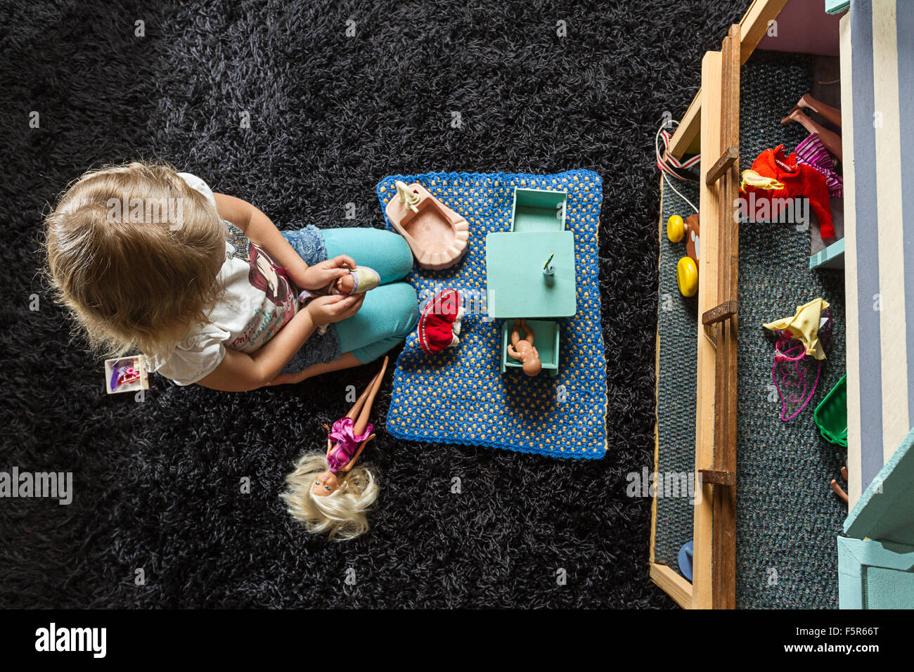 Little girl playing with dolls on a dark carpet inside at home. Stock Photo