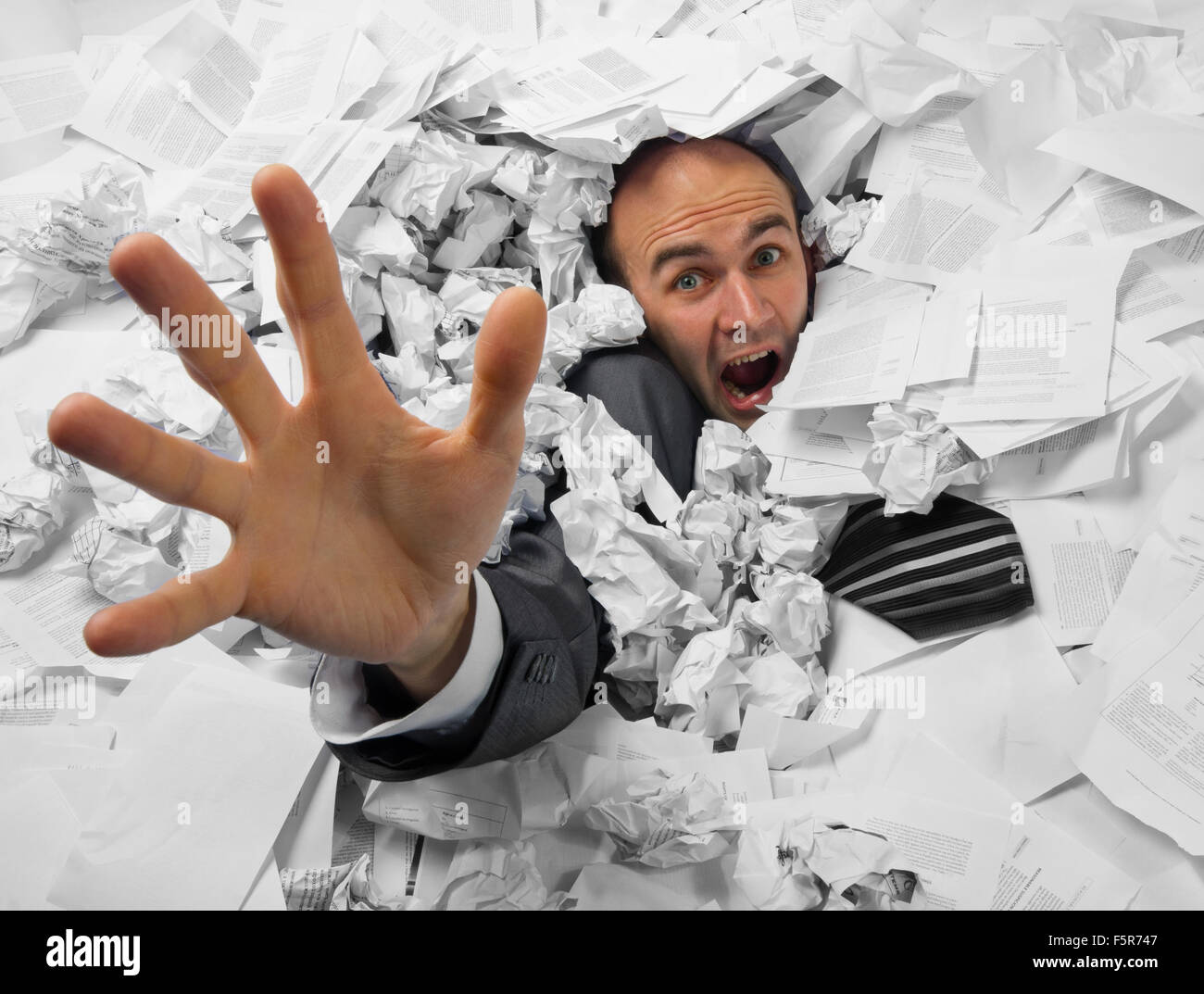 Businessman sinking in heap of documents and asking for help Stock Photo