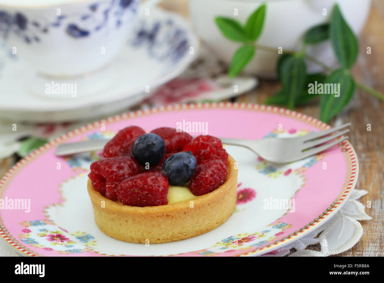 Delicious crunchy tartelette with custard, fresh raspberries and blueberries on pink plate Stock Photo