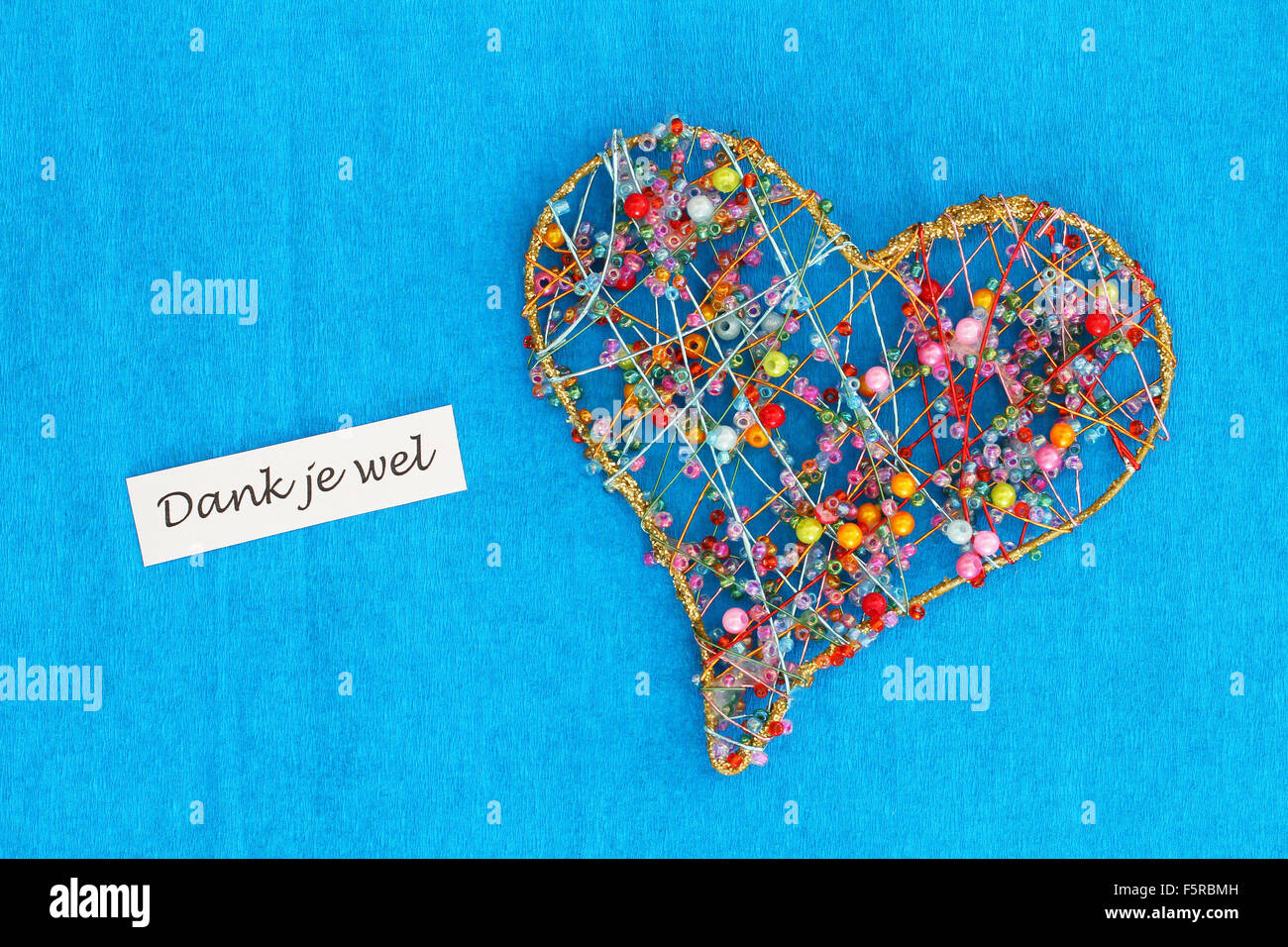 Dank je wel (which means thank you in Dutch) card with heart made of colorful beads on blue background Stock Photo