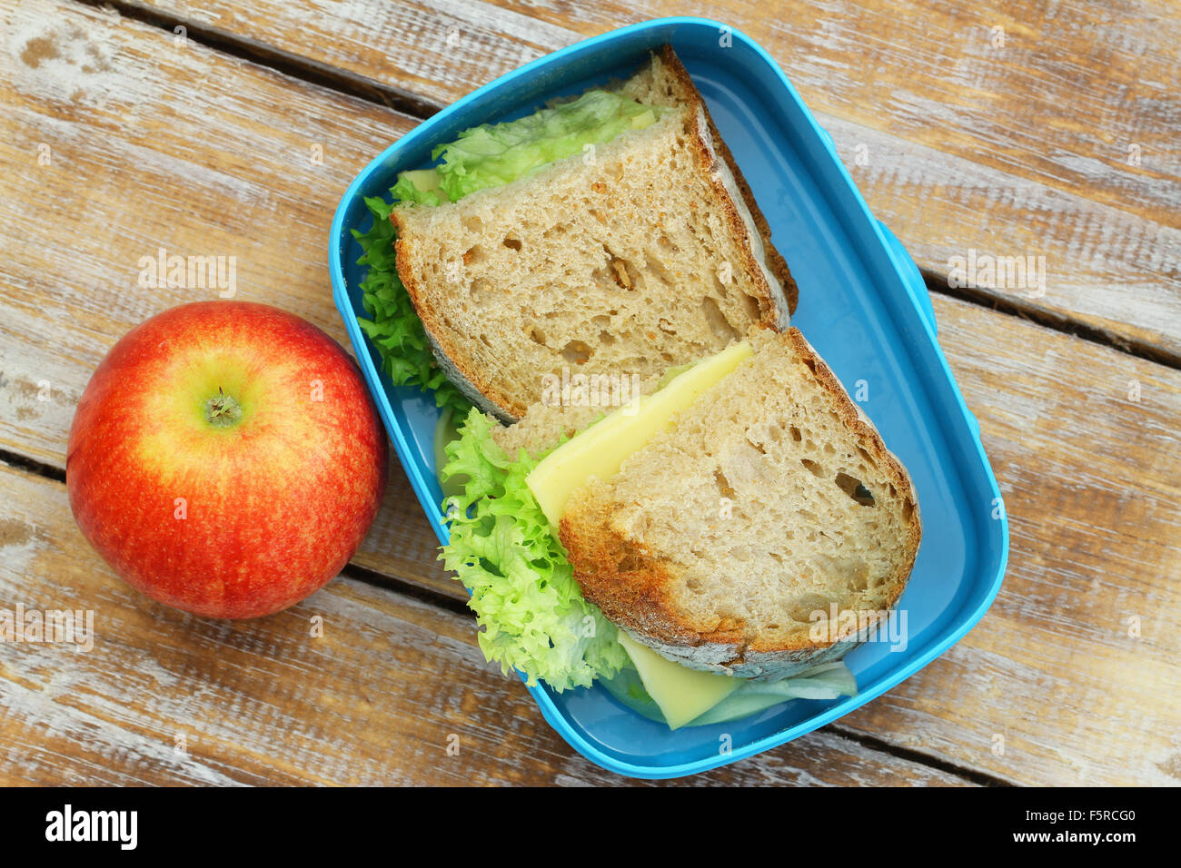 Healthy lunch box containing rustic bread sandwiches with cheese and lettuce and red apple Stock Photo