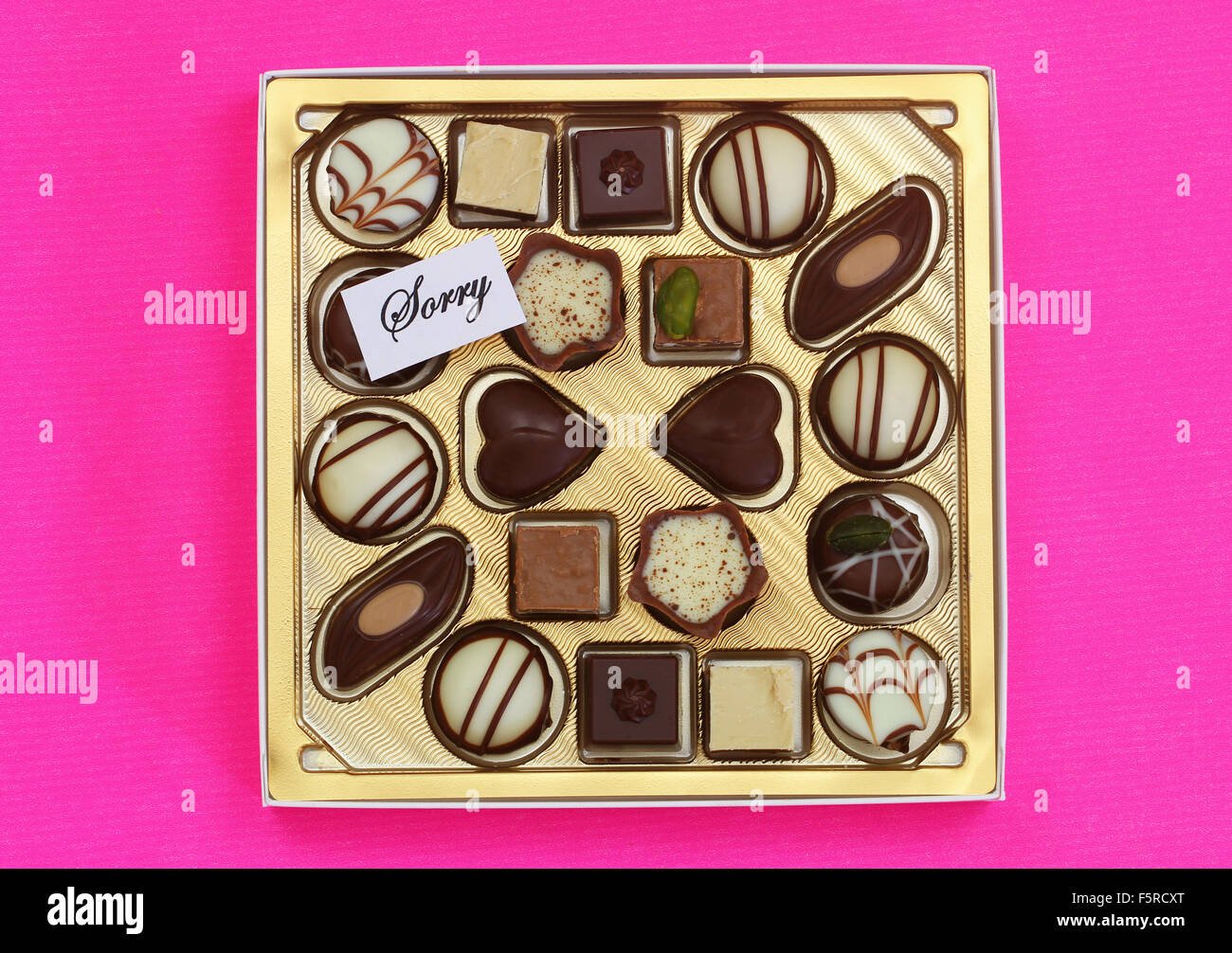 Sorry card with box of assorted chocolates on pink surface Stock Photo