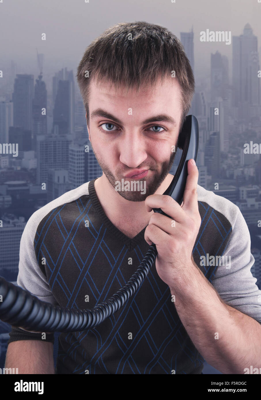 Bored young businessman talks on phone over city background Stock Photo