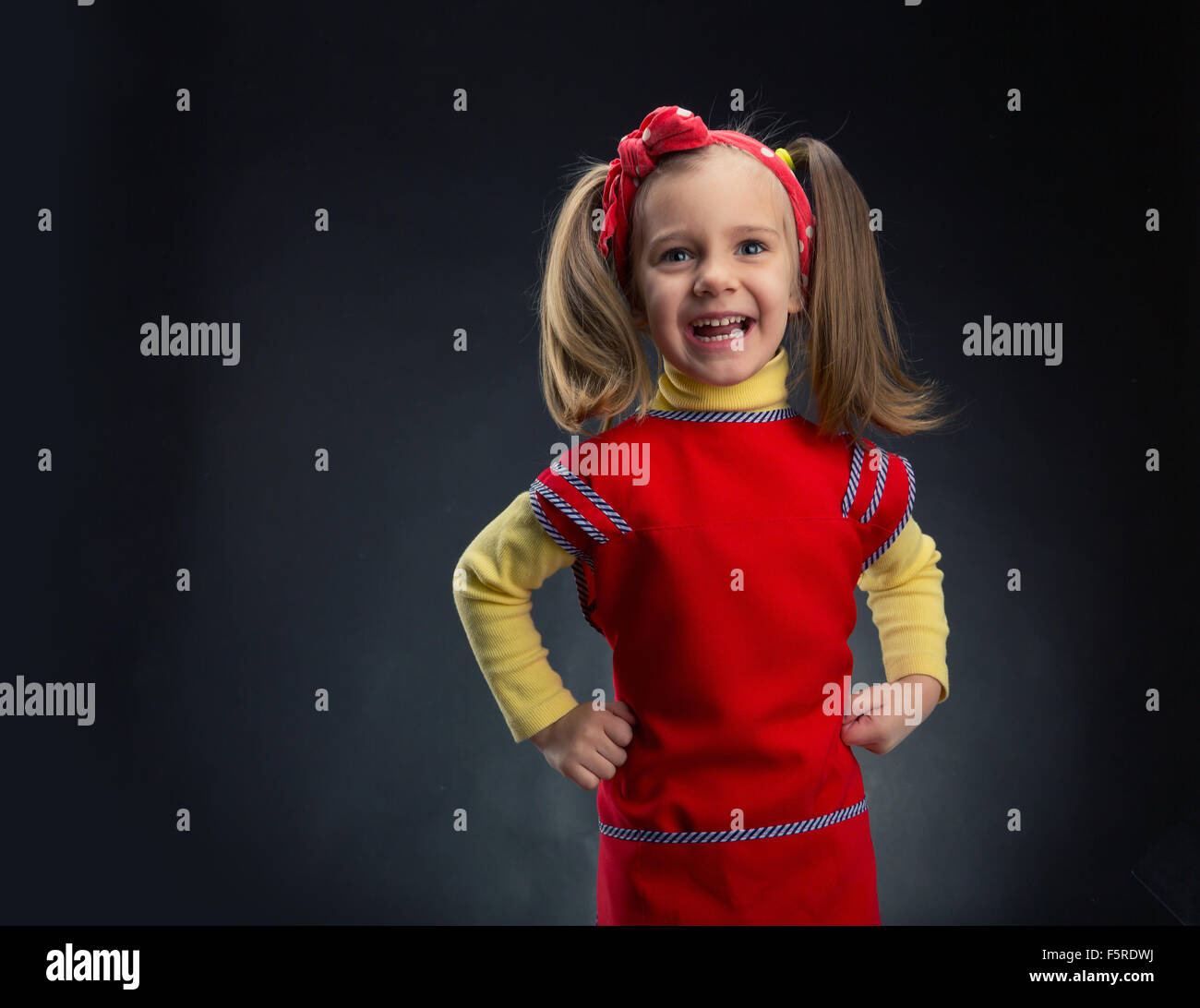 Cute little girl with her hands on hips smiling over grey background ...