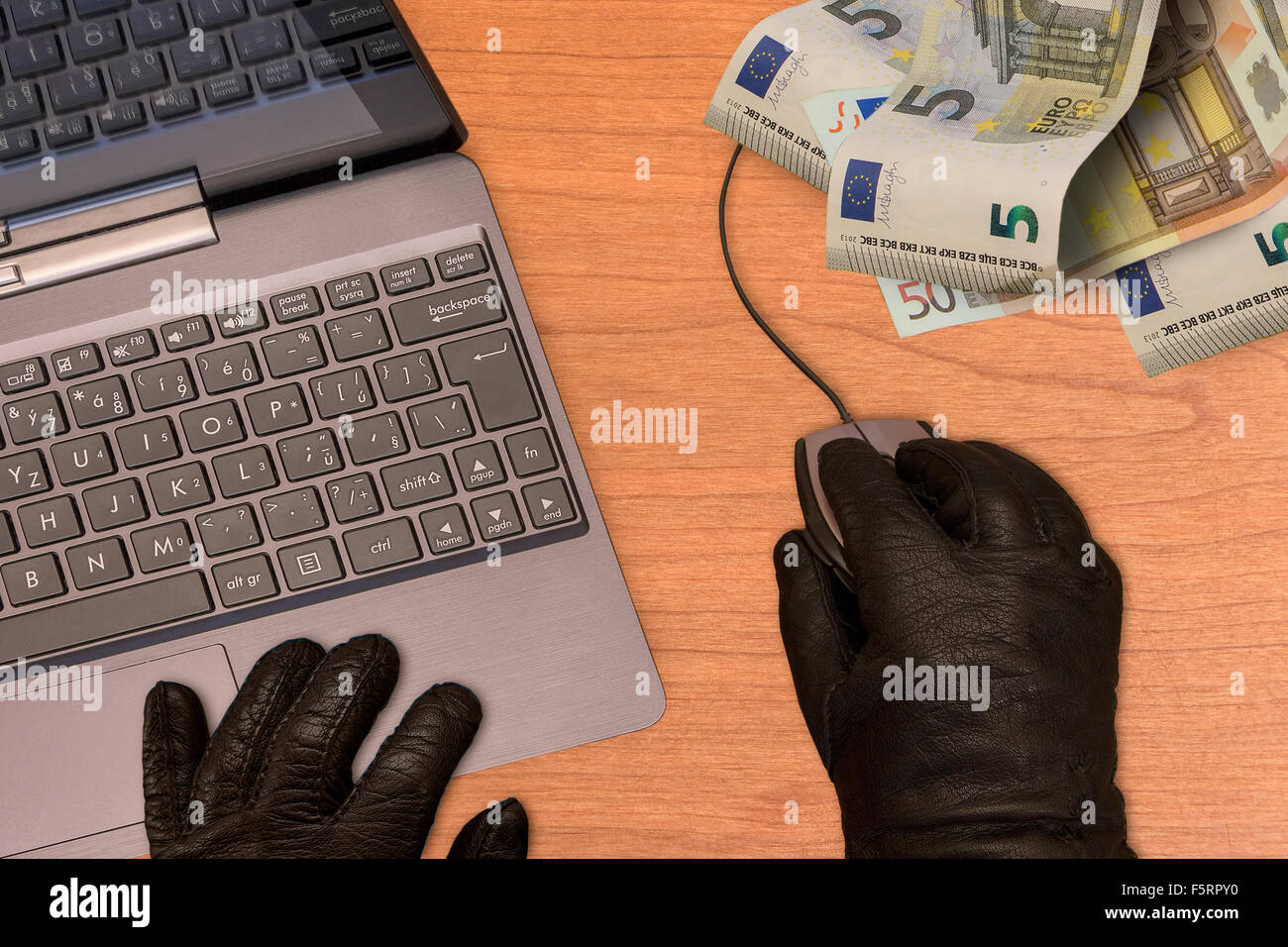 Computer crime metaphor, hand in black gloves with mouse, computer and banknotes. Stock Photo