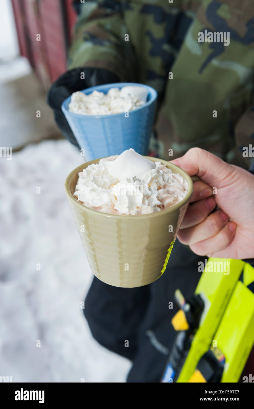 Sweden, Stockholm, Bjorkhagen, Hammarbybacken, Cropped view of man and woman holding mugs of hot chocolate with whipped cream Stock Photo