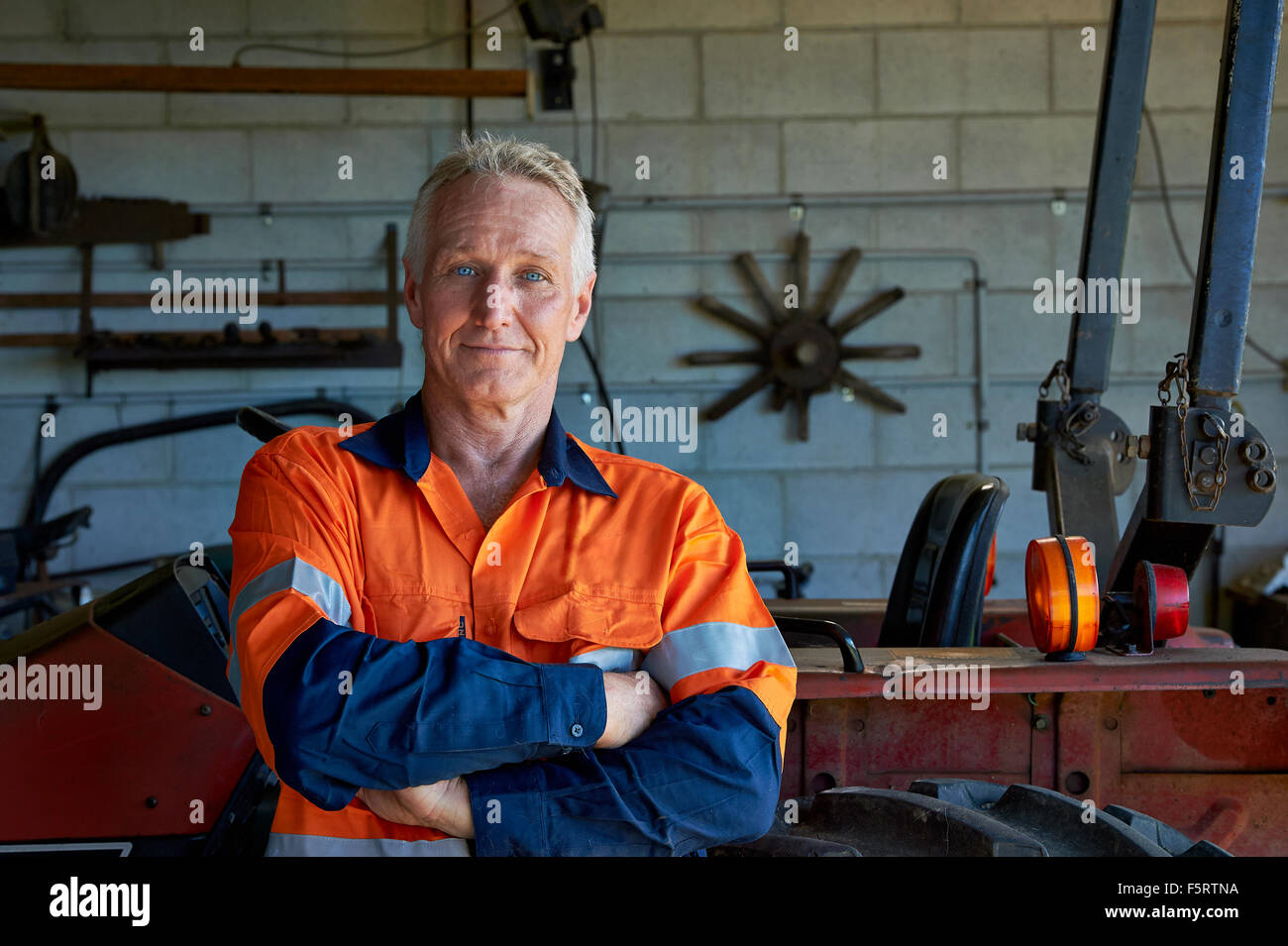 Mature aged man next to a tractor in his work shed. Stock Photo