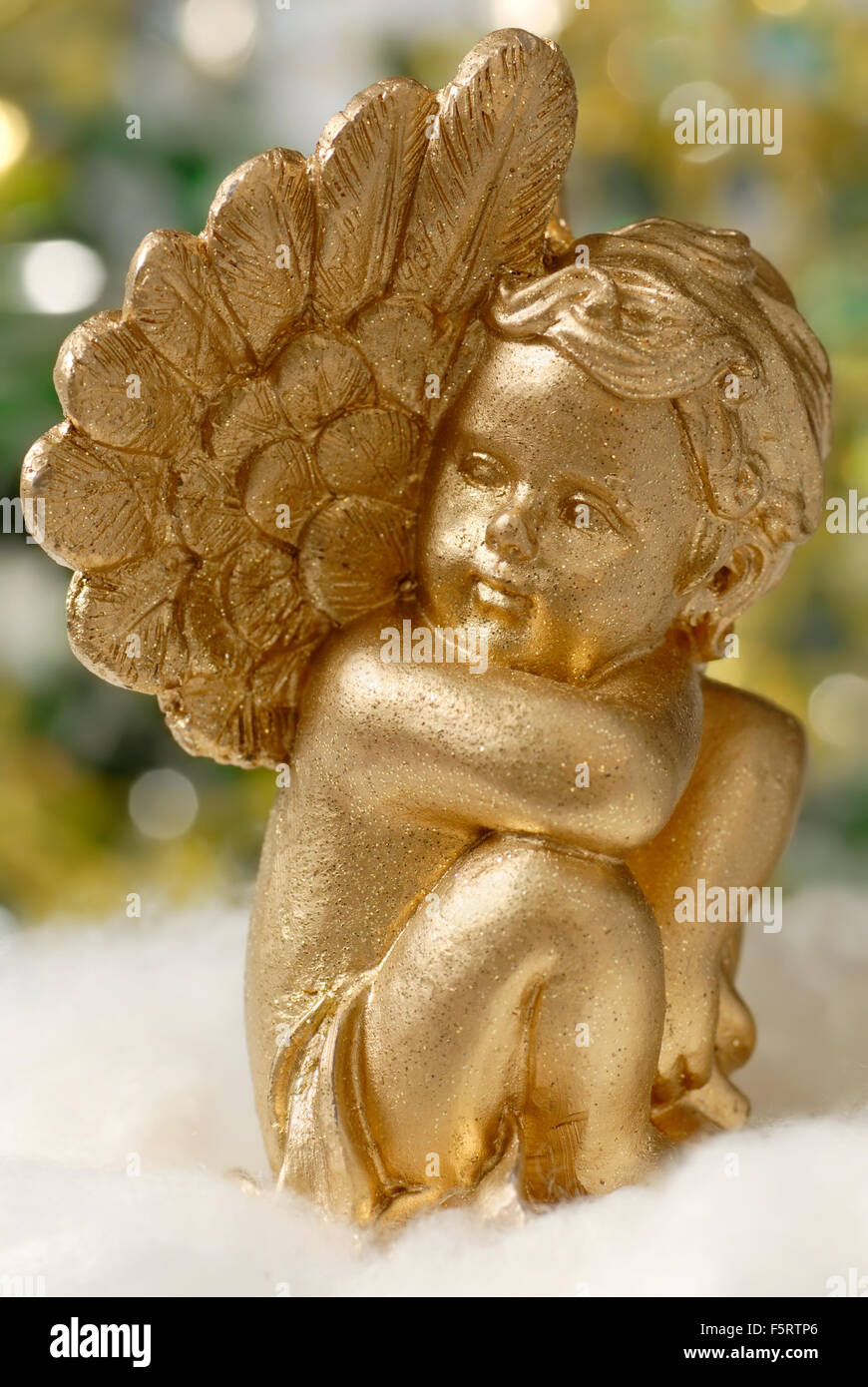 Golden angel figure on fluffy white material, with blurred lights in the background Stock Photo