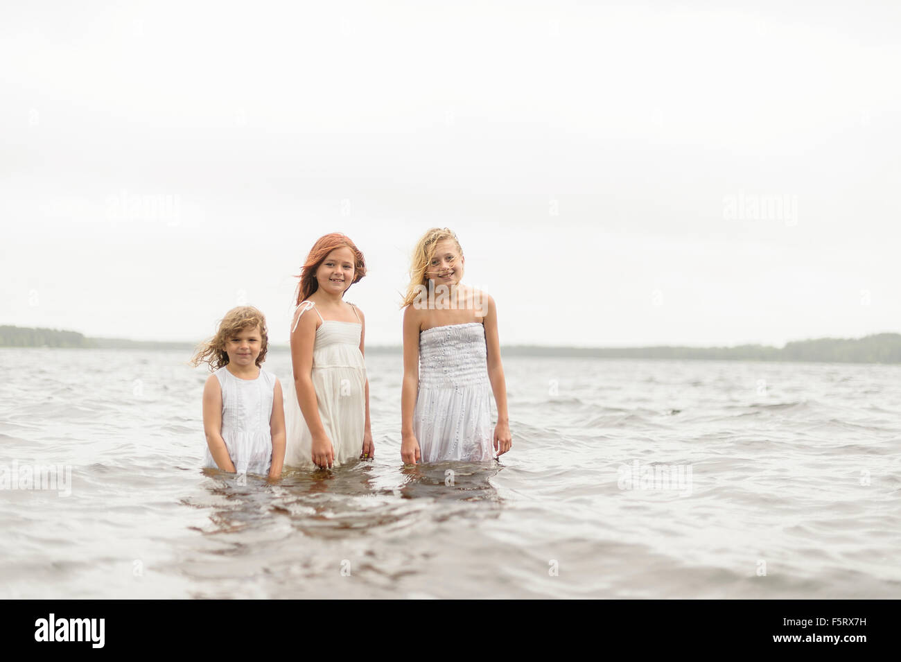 Sweden, Vastmanland, Bergslagen, Hallefors, Sangshyttan, Three girls (4-5, 8-9, 10-11) standing in water Stock Photo