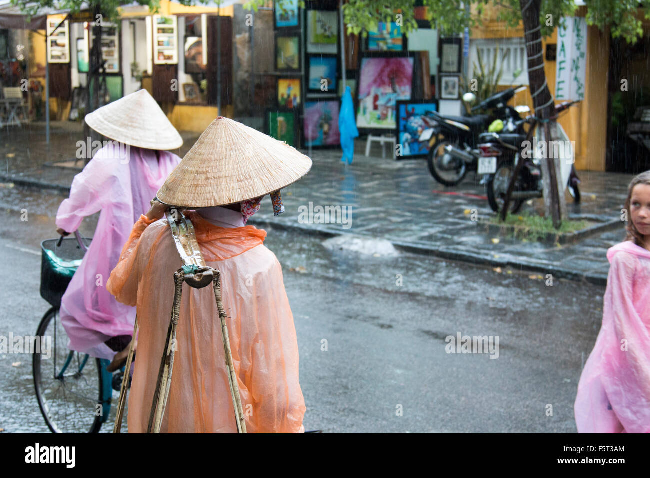 Hoi An old town in Vietnam. Wet season and heavy rains in the town. Young western tourist looking at vietnamese street vendor Stock Photo