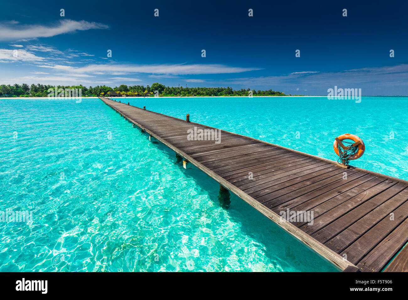 Long wooden jetty over atoll and a tropical resort island in Maldives ...