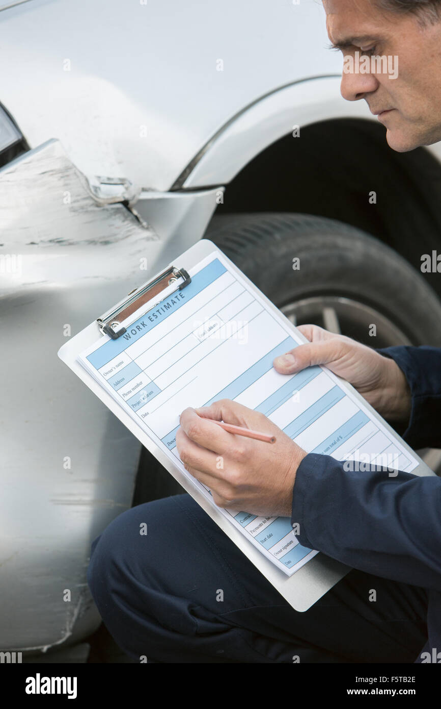Auto Workshop Mechanic Inspecting Damage To Car And Filling In Repair Estimate Stock Photo