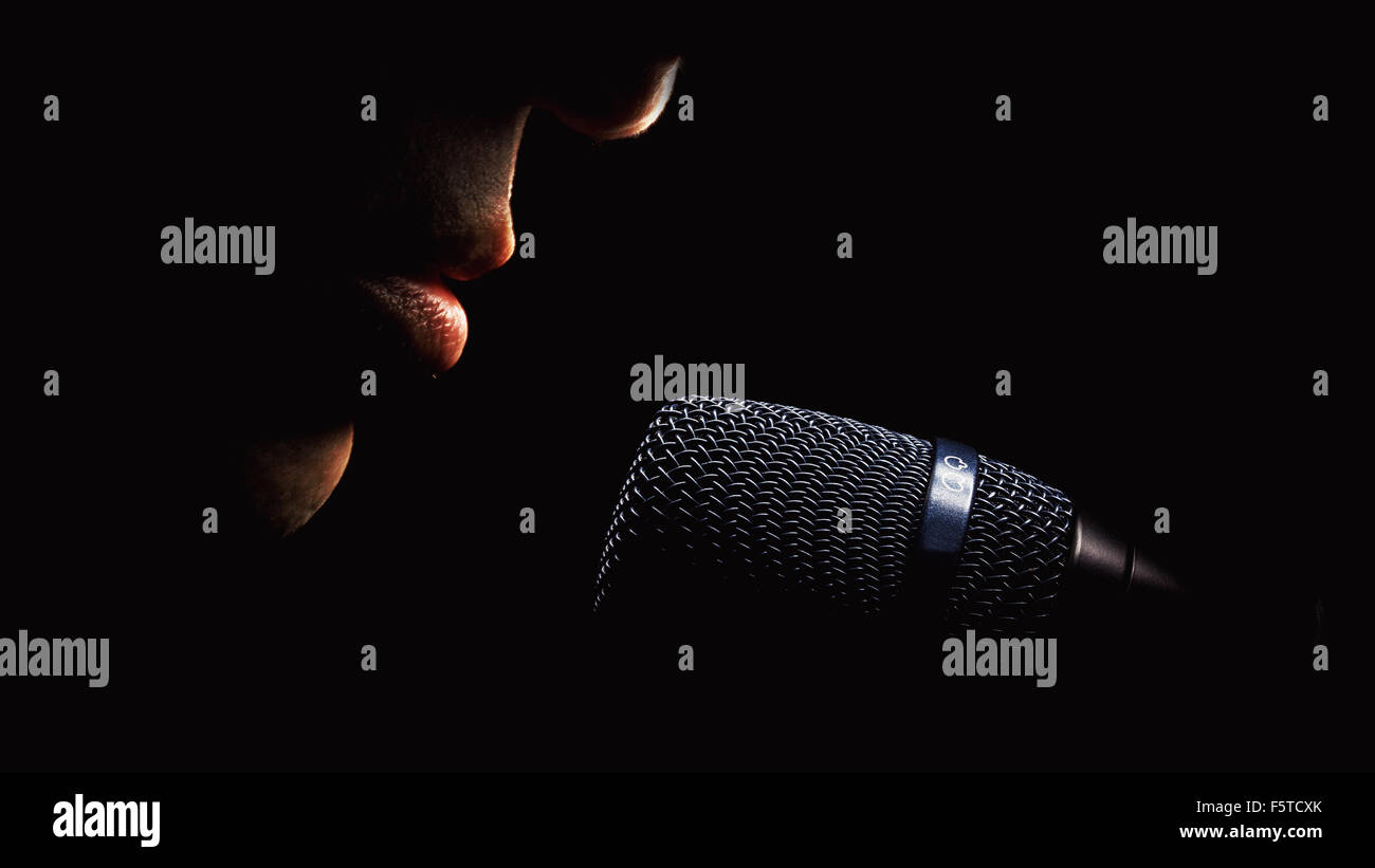 Part of a singer face, details of mouth and modern black microphone, on black background. Stock Photo